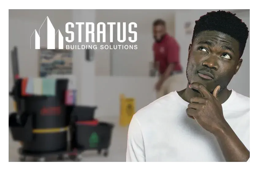 A man holding his hand to his chin while looking up with a quizzical expression with a janitor and janitorial supplies in the background.